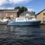 Vedette Salon Classic Line 36 ft, blauwe motorboot afgemeerd bij huizen