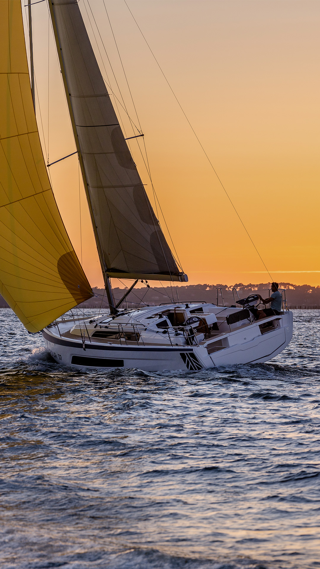 Dufour 37, zeilboot met gele spinnaker bij zonsondergang
